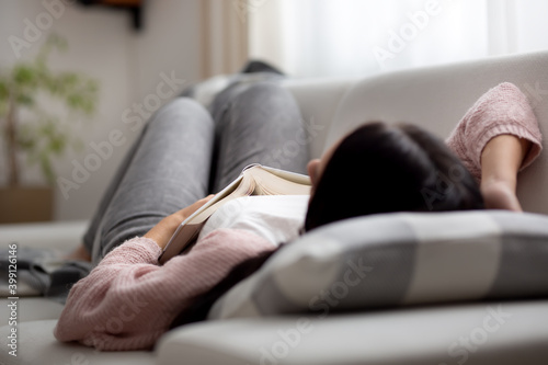 A woman falling asleep during the day on a couch while trying to read a book