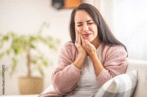 Obraz na płótnie Brunette sits at home with a toothache holding her right cheek with hands w salonie