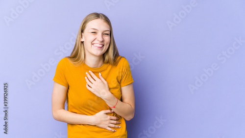 Foto Young blonde woman isolated on purple background laughs happily and has fun keeping hands on stomach
