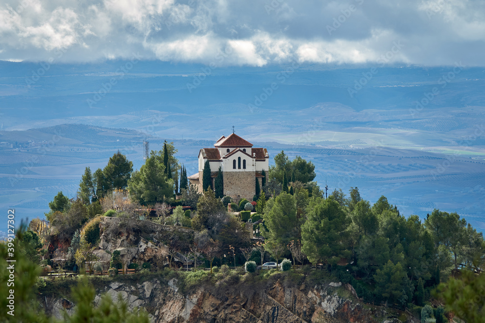 Hermitage of Tres Juanes (Granada) among pine trees on a high rock with the plain in the background on a cloudy day