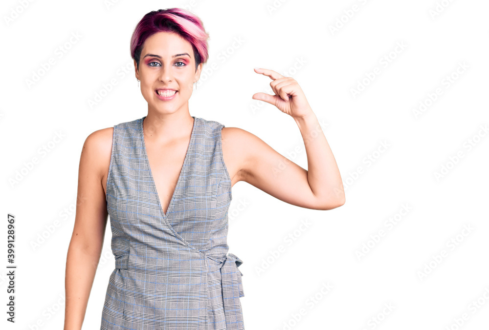 Young beautiful woman with pink hair wearing casual clothes smiling and confident gesturing with hand doing small size sign with fingers looking and the camera. measure concept. Young beautiful woman with pink hair wearing casual clothes smiling and confident gesturing with hand doing small size sign with fingers looking and the camera. measure concept.