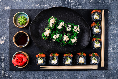 Sushi rolls set served on black stone slate on dark background, set Japanese sushi rolls with soy sauce, ginger and wasabi