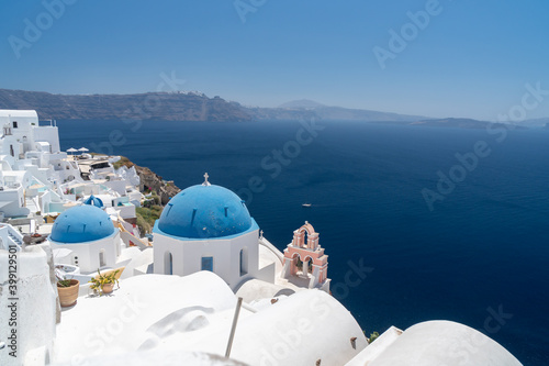 Famous Greek orthodox blue domed church and bell tower in Oia village on Santorini island, one of famous Greek Aegean Islands. Panoramic view from roof top