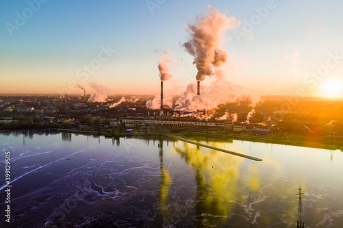 Industrial plant that works by burning gas with furnaces smoking abundantly at sunrise spreading thick clouds over the sky that polluting the the environment