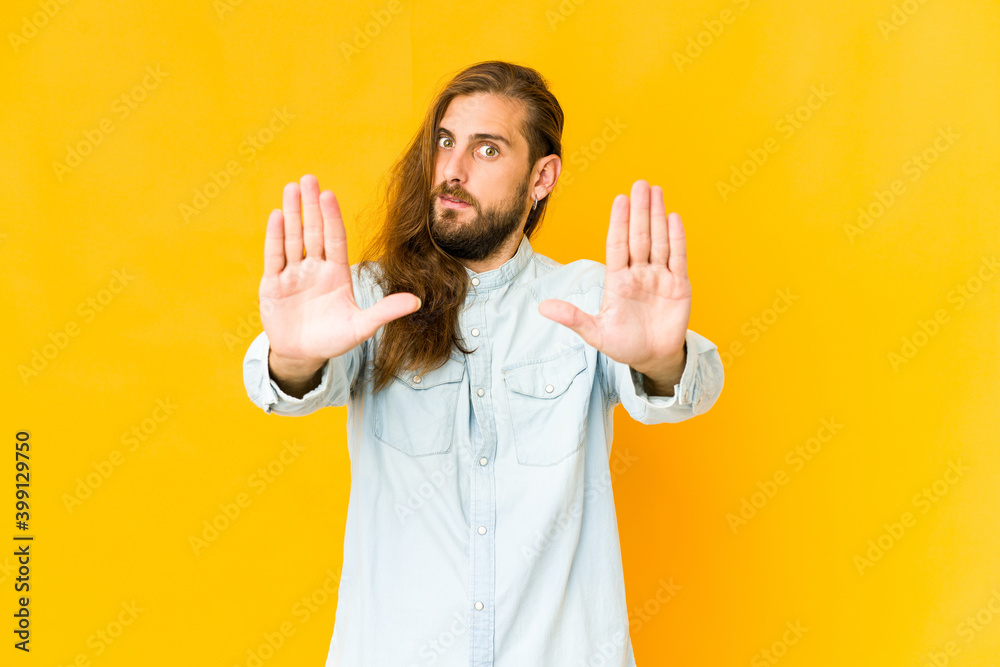 Young man with long hair look standing with outstretched hand showing stop sign, preventing you. Young man with long hair look standing with outstretched hand showing stop sign, preventing you.
