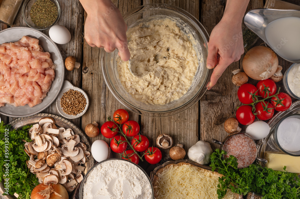 Fototapeta premium Chef mix ingredients with spoon in glass bowl for cooking dough on wooden table with variety of ingredients background. Concept of cooking process. Backstage of preparing pie. View from above.