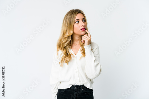 Young caucasian blonde woman looking sideways with doubtful and skeptical expression.