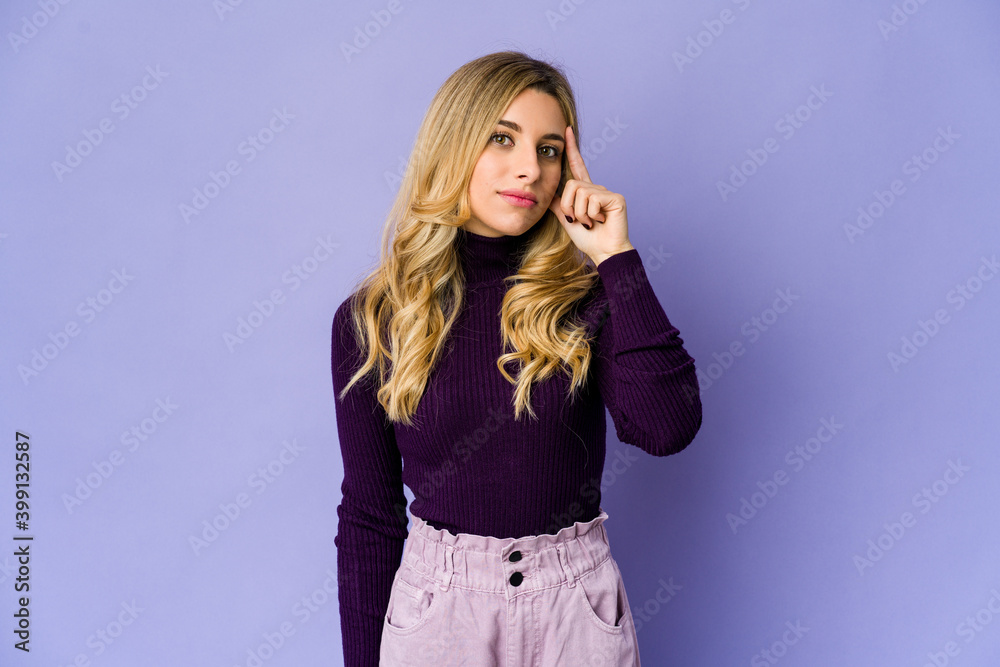 Young caucasian blonde woman pointing temple with finger, thinking, focused on a task.