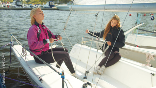 Two young sisters of a sailing sportswoman are preparing for a multi-day regatta on a sports yacht. Lay out the gear and tie knots on the ropes. © iaginzburg