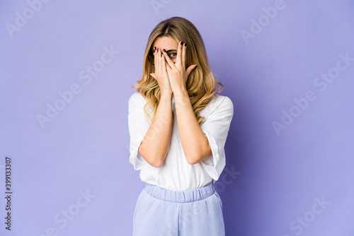 Young caucasian blonde woman blink through fingers frightened and nervous.