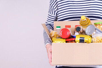 Volunteer hands holding food donations box with grocery products on white desk