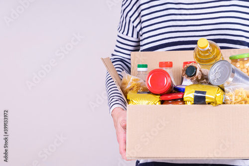 Obraz na plátně Volunteer hands holding food donations box with grocery products on white desk