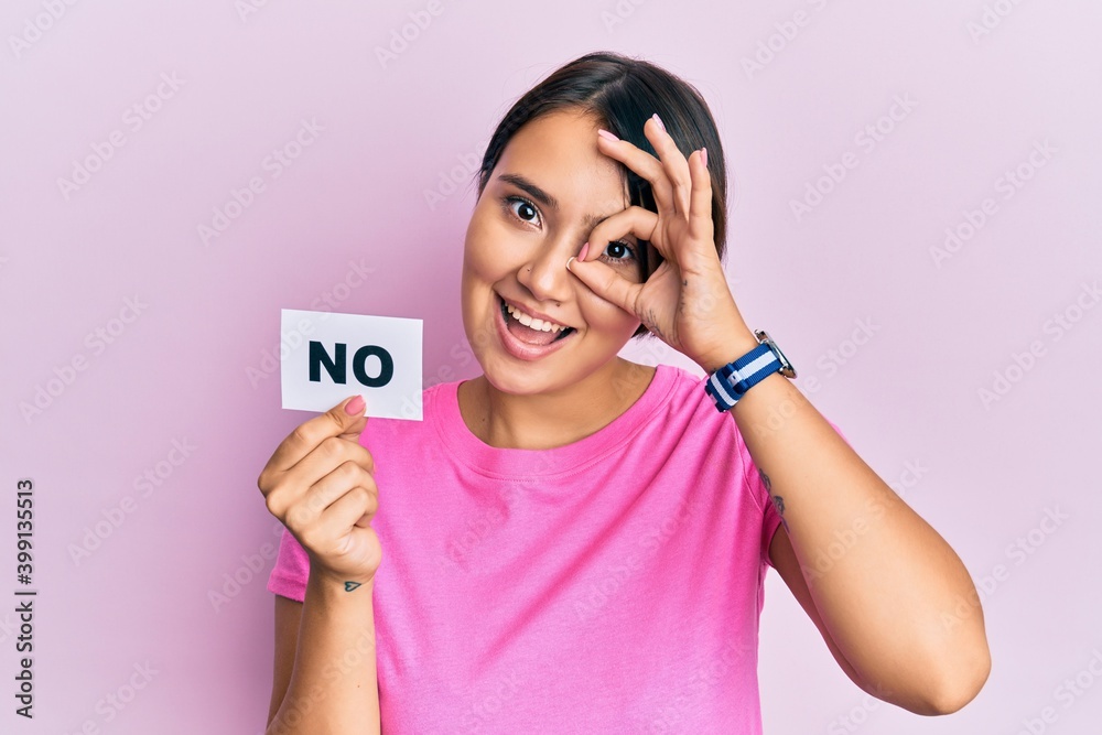 Beautiful young woman with short hair holding no word message smiling happy doing ok sign with hand on eye looking through fingers Beautiful young woman with short hair holding no word message smiling happy doing ok sign with hand on eye looking through fingers
