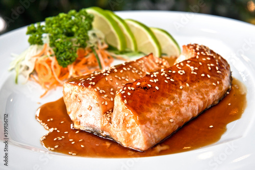 Grilled salmon teriyaki with vegetables and citrus Japanese food on white plate, on black background