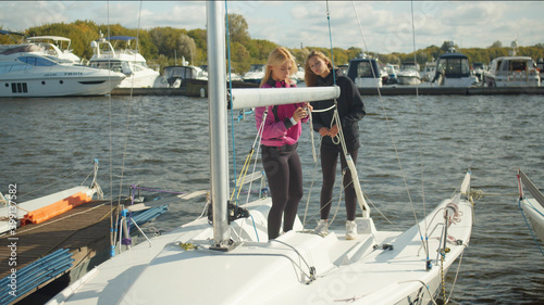 Two young friends are traveling on a yacht. They fasten the rigging and set the sails. Sports tourism concept.