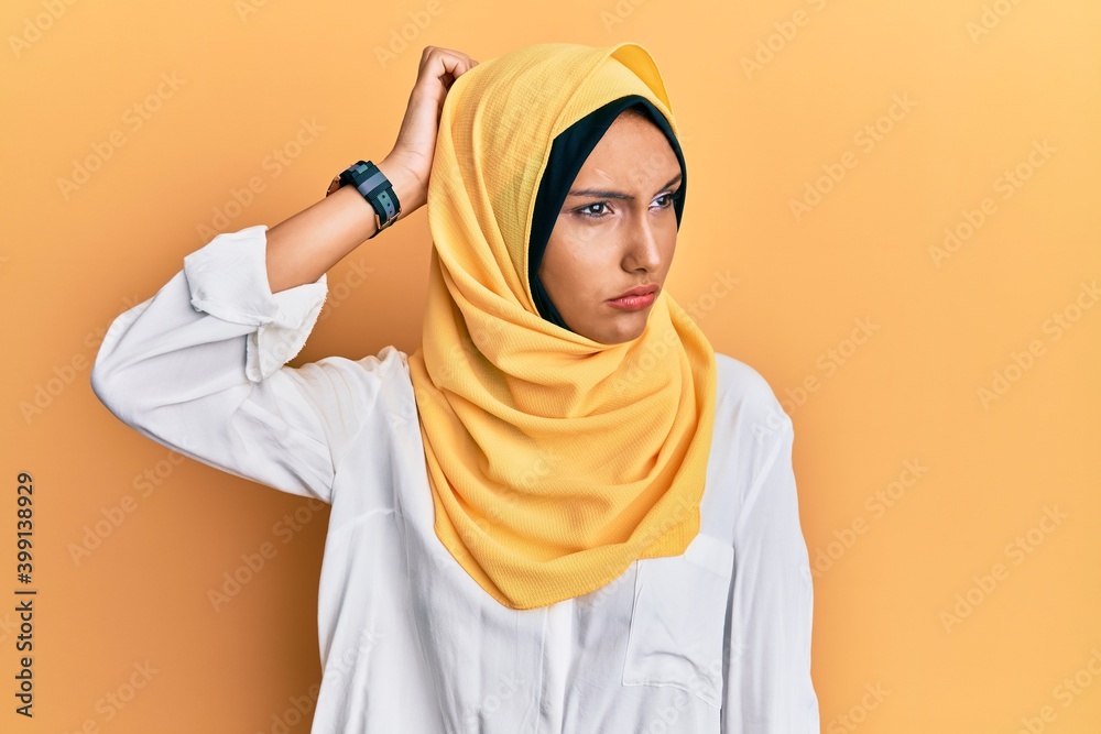 Obraz premium Young brunette arab woman wearing traditional islamic hijab scarf confuse and wondering about question. uncertain with doubt, thinking with hand on head. pensive concept.