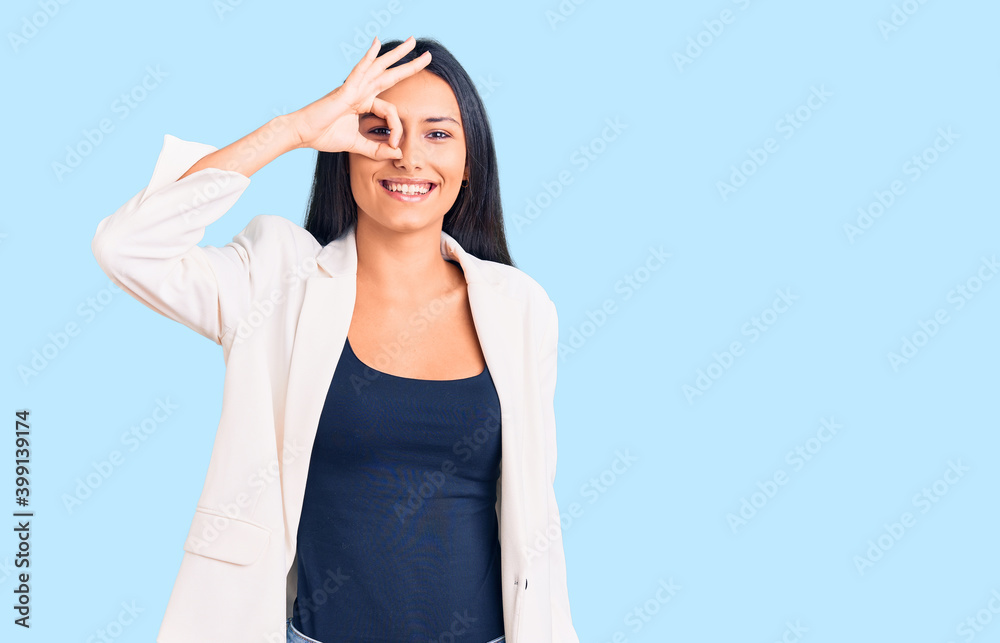 Young beautiful latin girl wearing business clothes smiling happy doing ok sign with hand on eye looking through fingers Young beautiful latin girl wearing business clothes smiling happy doing ok sign with hand on eye looking through fingers