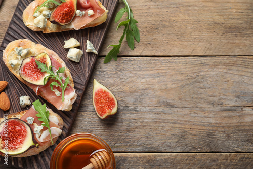 Sandwiches with ripe figs and prosciutto served on wooden table, flat lay. Space for text