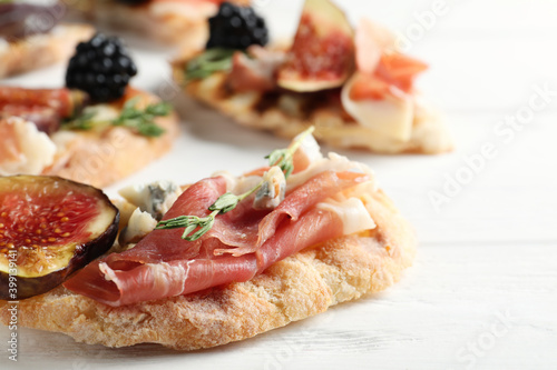 Sandwich with ripe figs and prosciutto served on white wooden table, closeup