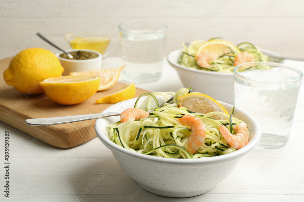 Delicious zucchini pasta with shrimps and lemon in bowl served on white wooden table