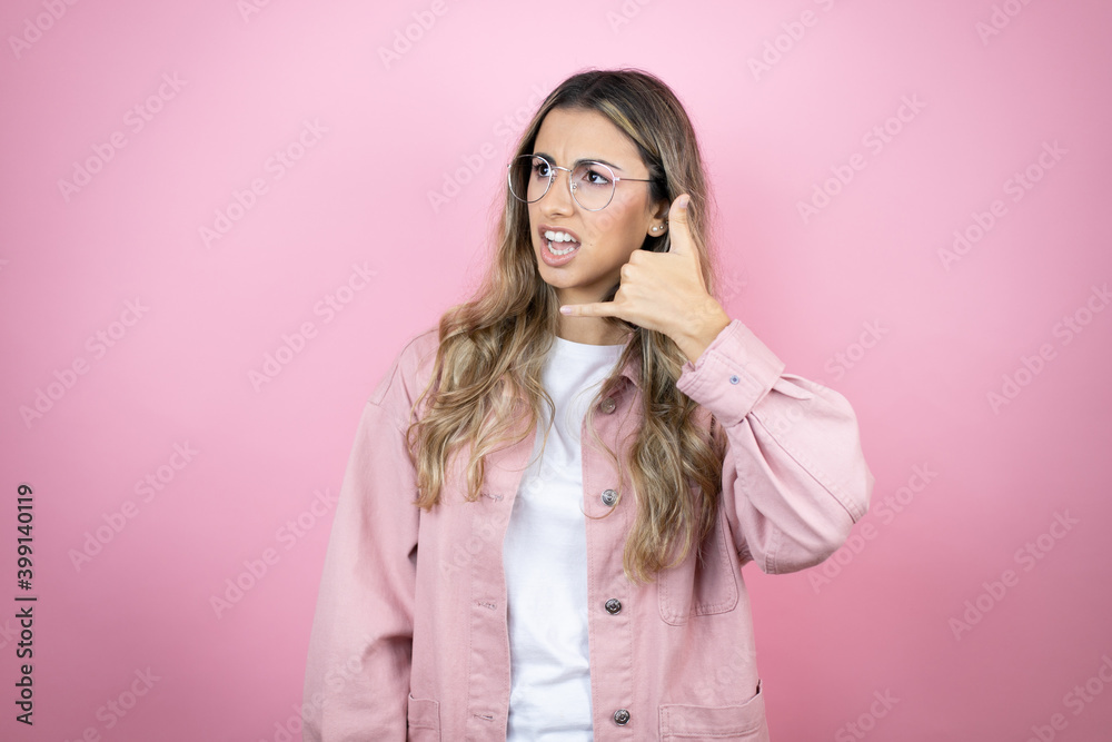 Young beautiful blonde woman with long hair standing over pink background onfused doing phone gesture with hand and fingers like talking on the telephone Young beautiful blonde woman with long hair standing over pink background onfused doing phone gesture with hand and fingers like talking on the telephone