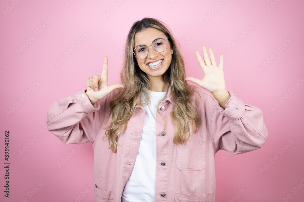 Young beautiful blonde woman with long hair standing over pink background showing and pointing up with fingers number seven while smiling confident and happy