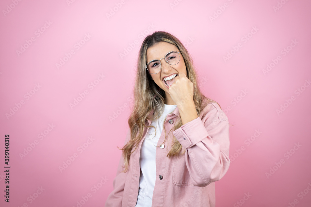 Young beautiful blonde woman with long hair standing over pink background angry and mad raising fist frustrated and furious while shouting with anger. Rage and aggressive concept. Young beautiful blonde woman with long hair standing over pink background angry and mad raising fist frustrated and furious while shouting with anger. Rage and aggressive concept.