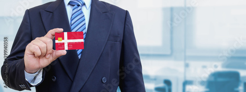 Cropped image of businessman holding plastic credit card with printed flag of Denmark. Background blurred. photo