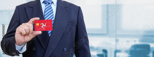 Cropped image of businessman holding plastic credit card with printed flag of Isle of Man. Background blurred. photo