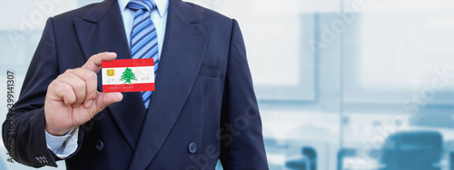 Cropped image of businessman holding plastic credit card with printed flag of Lebanon. Background blurred. photo