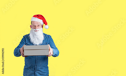courier in a blue denim shirt and santa claus hat with boxes in his hands on a yellow background
