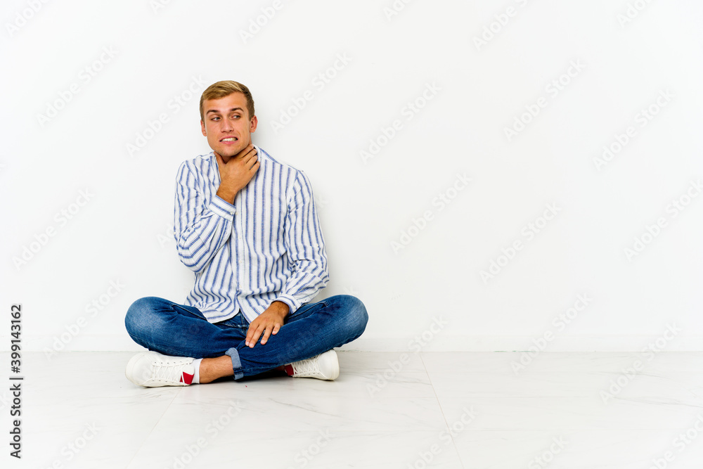 Young caucasian man sitting on the floor touching back of head, thinking and making a choice. Young caucasian man sitting on the floor touching back of head, thinking and making a choice.