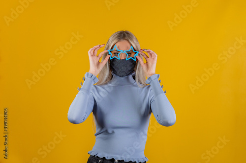 Portrait of funny pretty young woman wearing medical mask and funny glasses on yellow background. Conceptual photo of symbolizing the epidemic of the coronavirus © damianobuffo