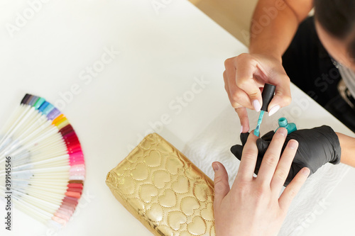 Latin manicurist in process of doing manicure to female customer in beauty salon, wearing gloves for security measures. Manicure and beauty salon concept. Copy space. photo