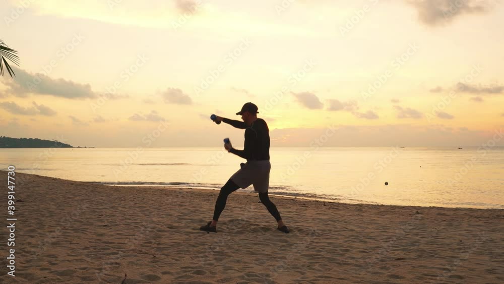 Silhouette of a man doing shadow boxing with dumbbells on the beach by the sea at sunrise Silhouette of a man doing shadow boxing with dumbbells on the beach by the sea at sunrise