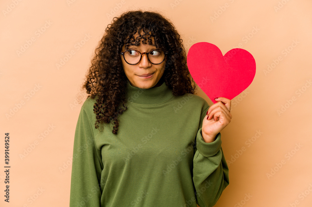Young african american afro woman holding a valentines day heart confused, feels doubtful and unsure.