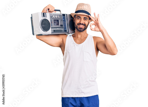 Young hispanic man holding boombox, listening to music doing ok sign with fingers, smiling friendly gesturing excellent symbol