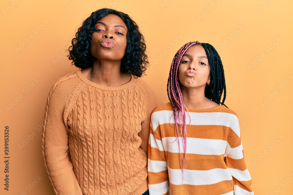 Beautiful african american mother and daughter wearing wool winter sweater looking at the camera blowing a kiss on air being lovely and sexy. love expression. Beautiful african american mother and daughter wearing wool winter sweater looking at the camera blowing a kiss on air being lovely and sexy. love expression.