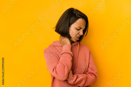 Young hispanic woman isolated on yellow having a neck pain due to stress, massaging and touching it with hand.