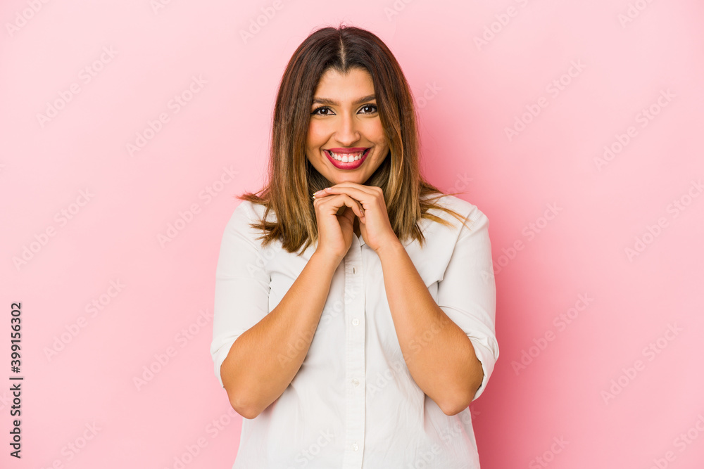 Young indian woman isolated on pink background keeps hands under chin, is looking happily aside. Young indian woman isolated on pink background keeps hands under chin, is looking happily aside.