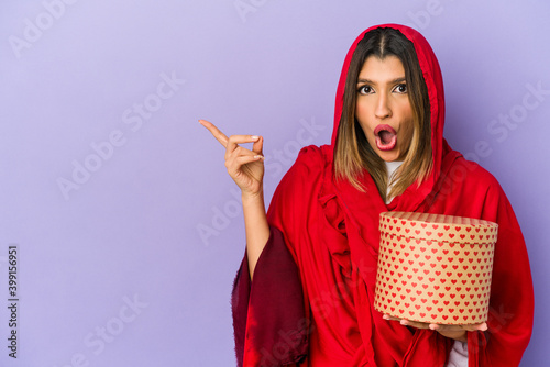 Young indian woman wearing a hijab holding a valentines day gift isolated pointing to the side