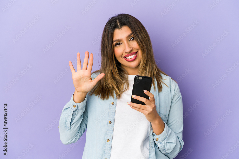 Young indian woman holding a phone isolated smiling cheerful showing number five with fingers. Young indian woman holding a phone isolated smiling cheerful showing number five with fingers.