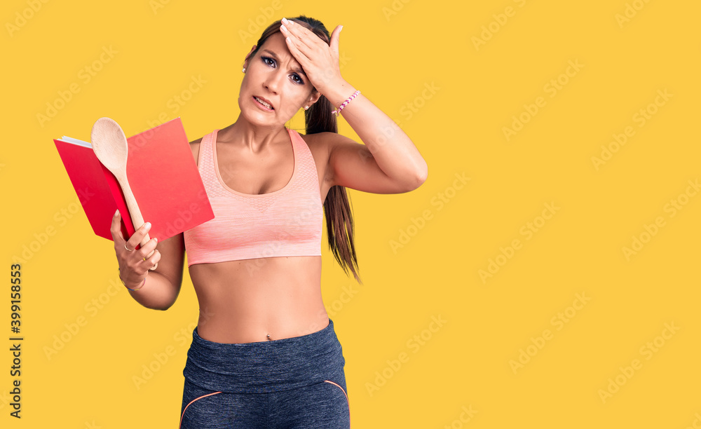 Young beautiful hispanic woman wearing gym clothes reading cooking recipe book holding spoon stressed and frustrated with hand on head, surprised and angry face Young beautiful hispanic woman wearing gym clothes reading cooking recipe book holding spoon stressed and frustrated with hand on head, surprised and angry face