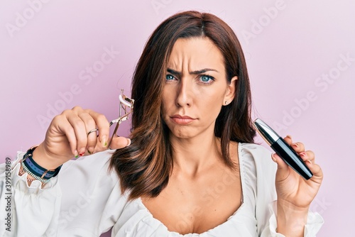 Young brunette woman holding eyelash curler skeptic and nervous, frowning upset because of problem. negative person.