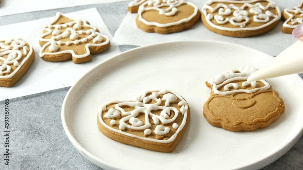 Decorating holiday gingerbread cookie. Pastry bag with white icing. Making handmade festive new cookies for gift in shape of santa claus and heart. Christmas and new year traditions.