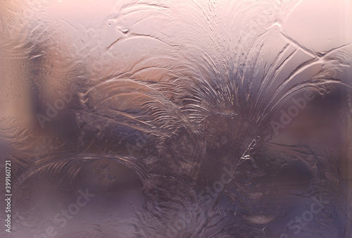 frosty patterns on the window with sunset light and sky - close up, winter background and icy plants