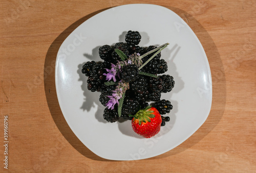 Plate of blackberries with a strawberry, accompanied by labanda flowers, on a white plate photo