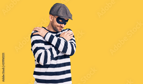 Young handsome man wearing burglar mask hugging oneself happy and positive, smiling confident. self love and self care © Krakenimages.com