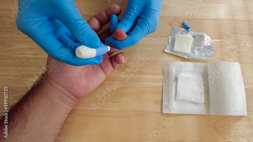 Фотография A medical personnel wearing gloves is performing a finger prick blood draw at a clinic using a disposable single use lancet