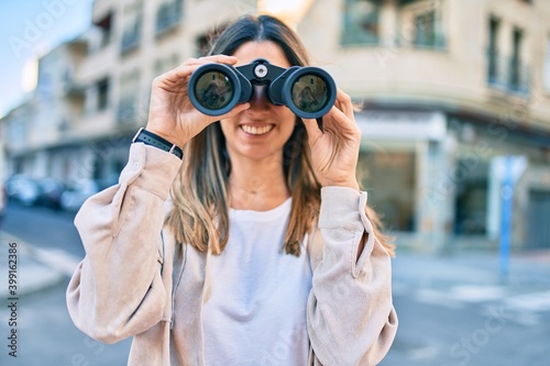 Young caucasian woman smiling happy looking for new opportunity using binoculars walking at the city. © Krakenimages.com
